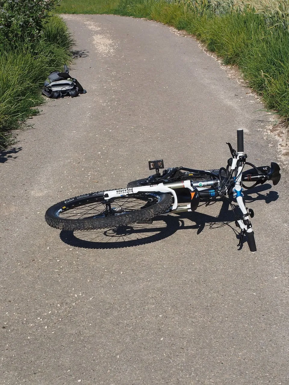 Wegeunfall? Fahrrad liegt auf asphaltierter Landstraße neben Rucksack.